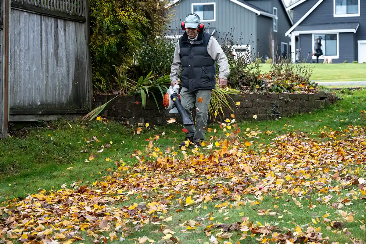 man in fall clothing cleaning up leaves in yard